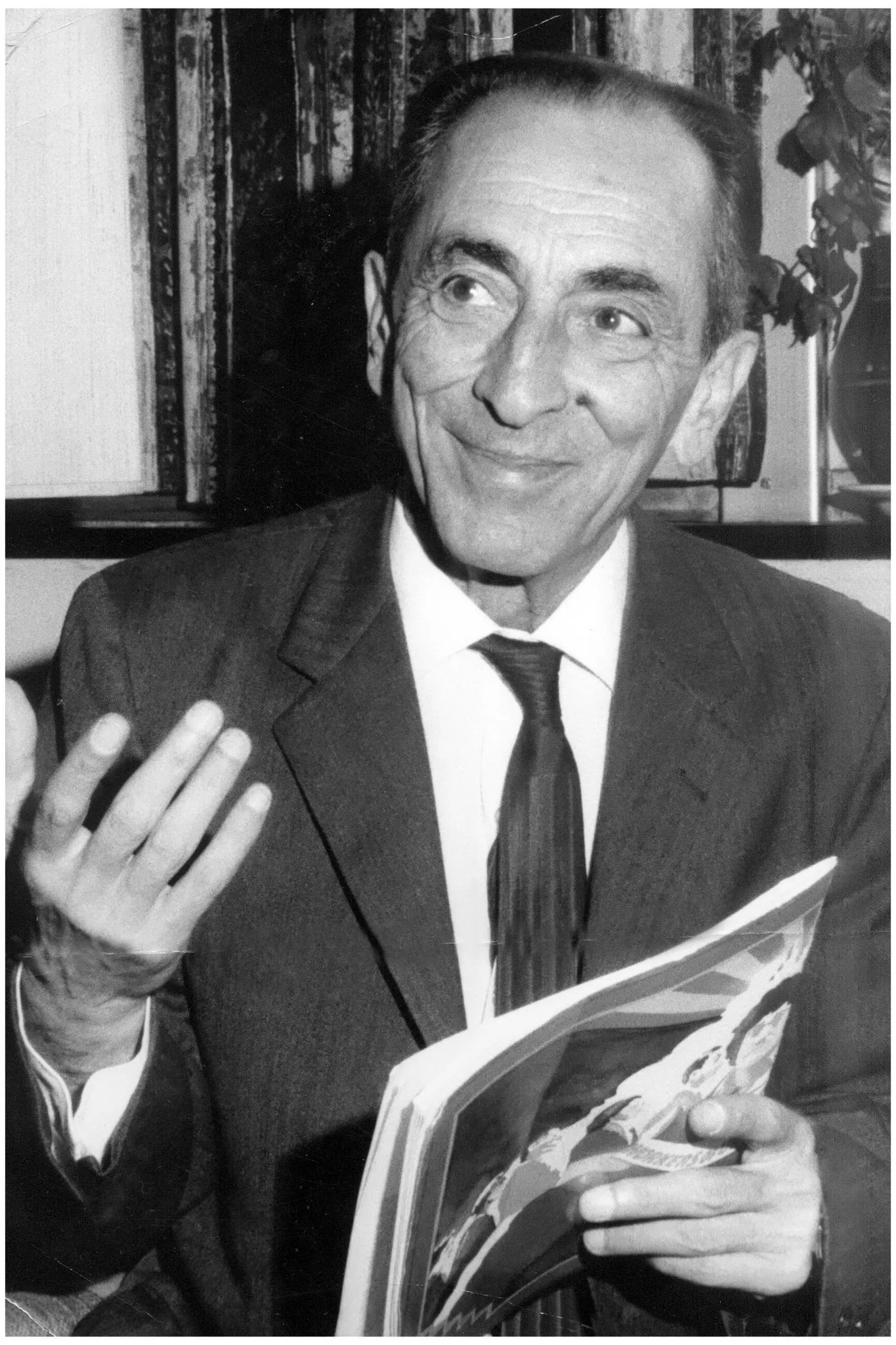 Un homme aux cheveux gris en costume, un programme à la main, en noir et blanc.