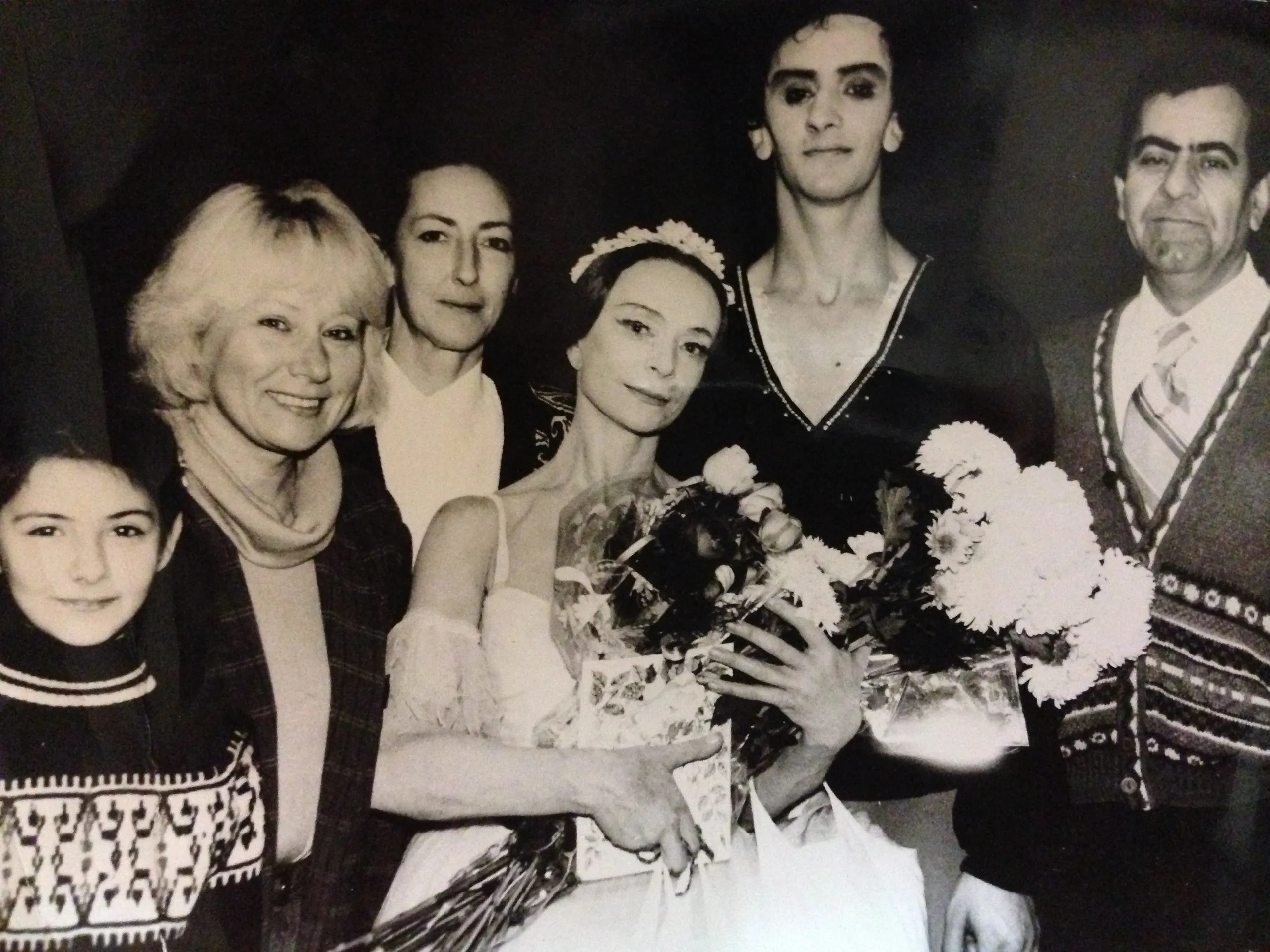 Après le spectacle : un groupe en costume entoure une danseuse aux fleurs, en noir et blanc.