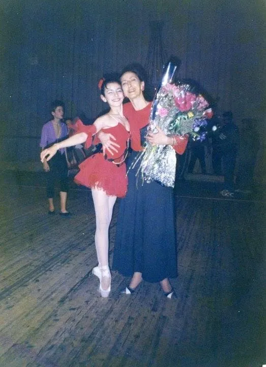 Jeune danseuse en costume rouge, des fleurs à la main, aux côtés de son partenaire.