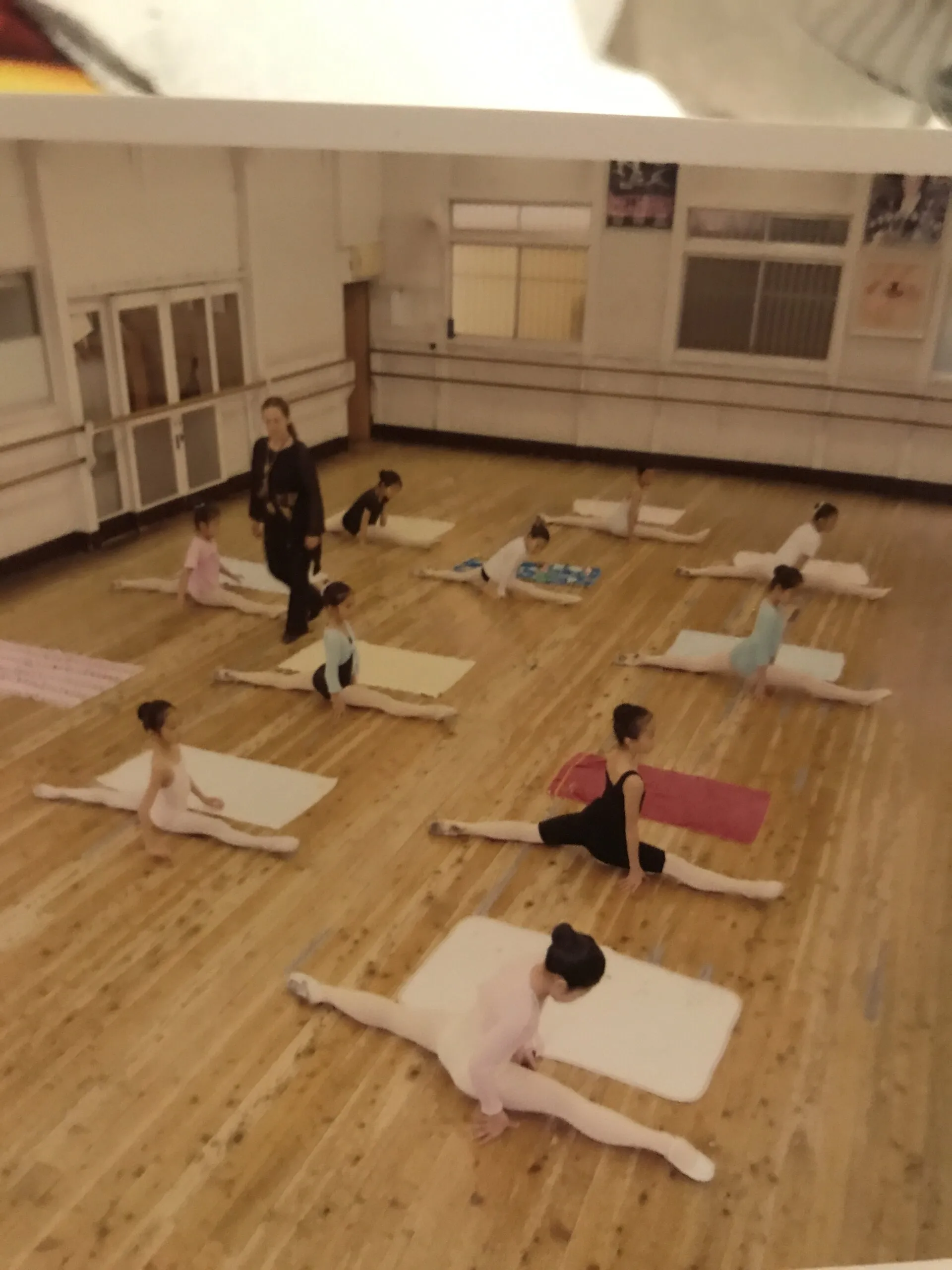 Des élèves travaillent les assouplissements sur des tapis, dans un grand studio clair.