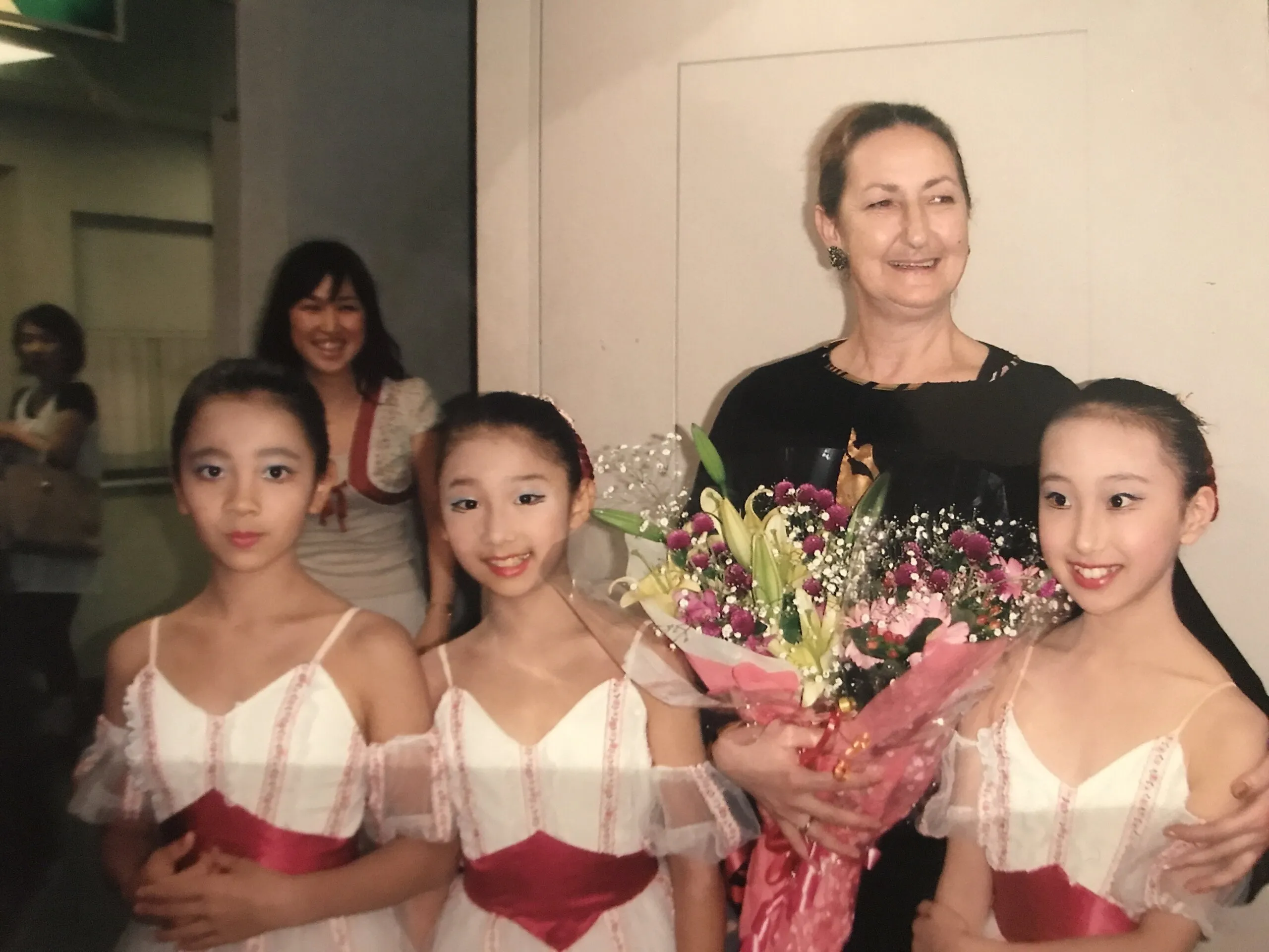Trois élèves en costume de scène entourent leur professeure, un bouquet dans les bras.