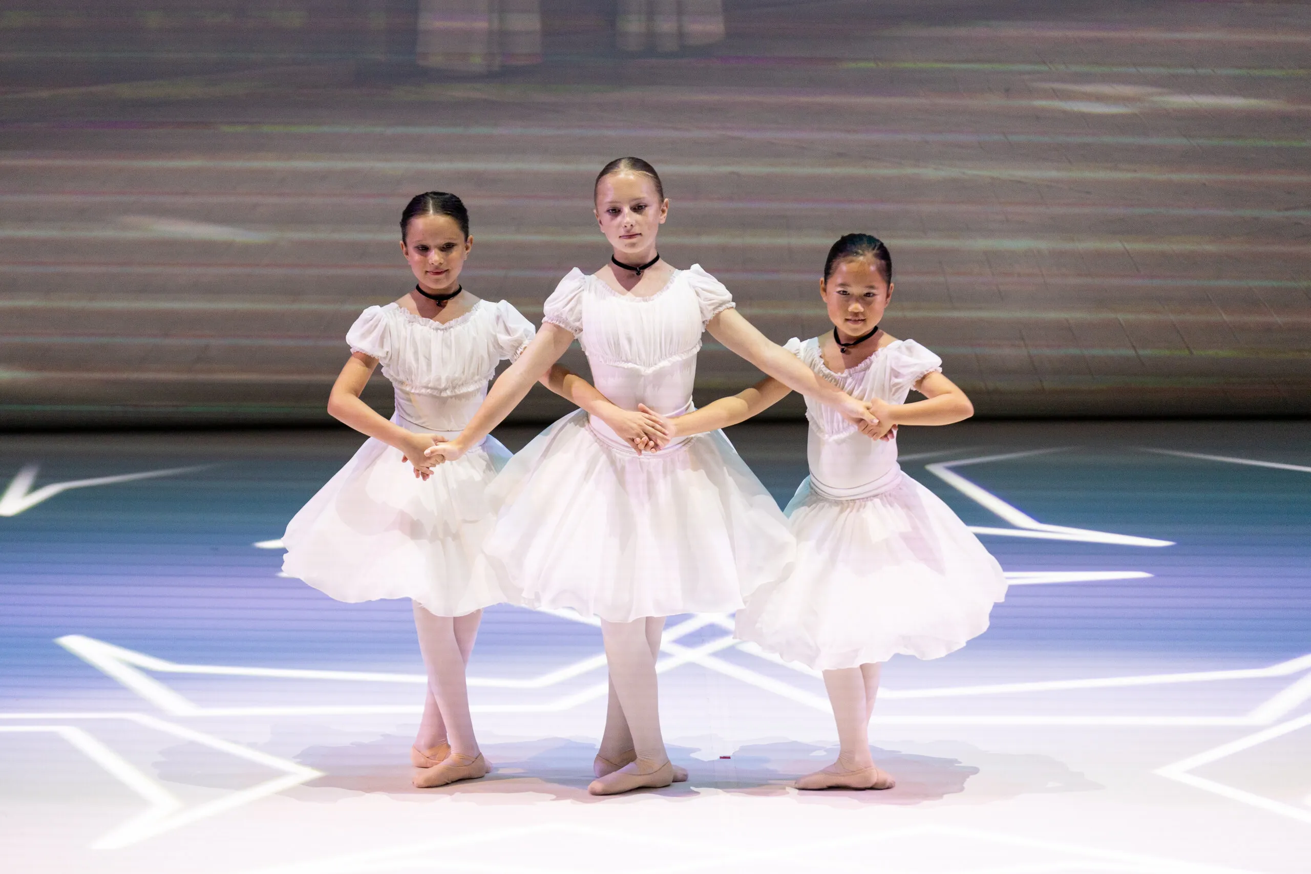 Three students in white dresses, hands joined.