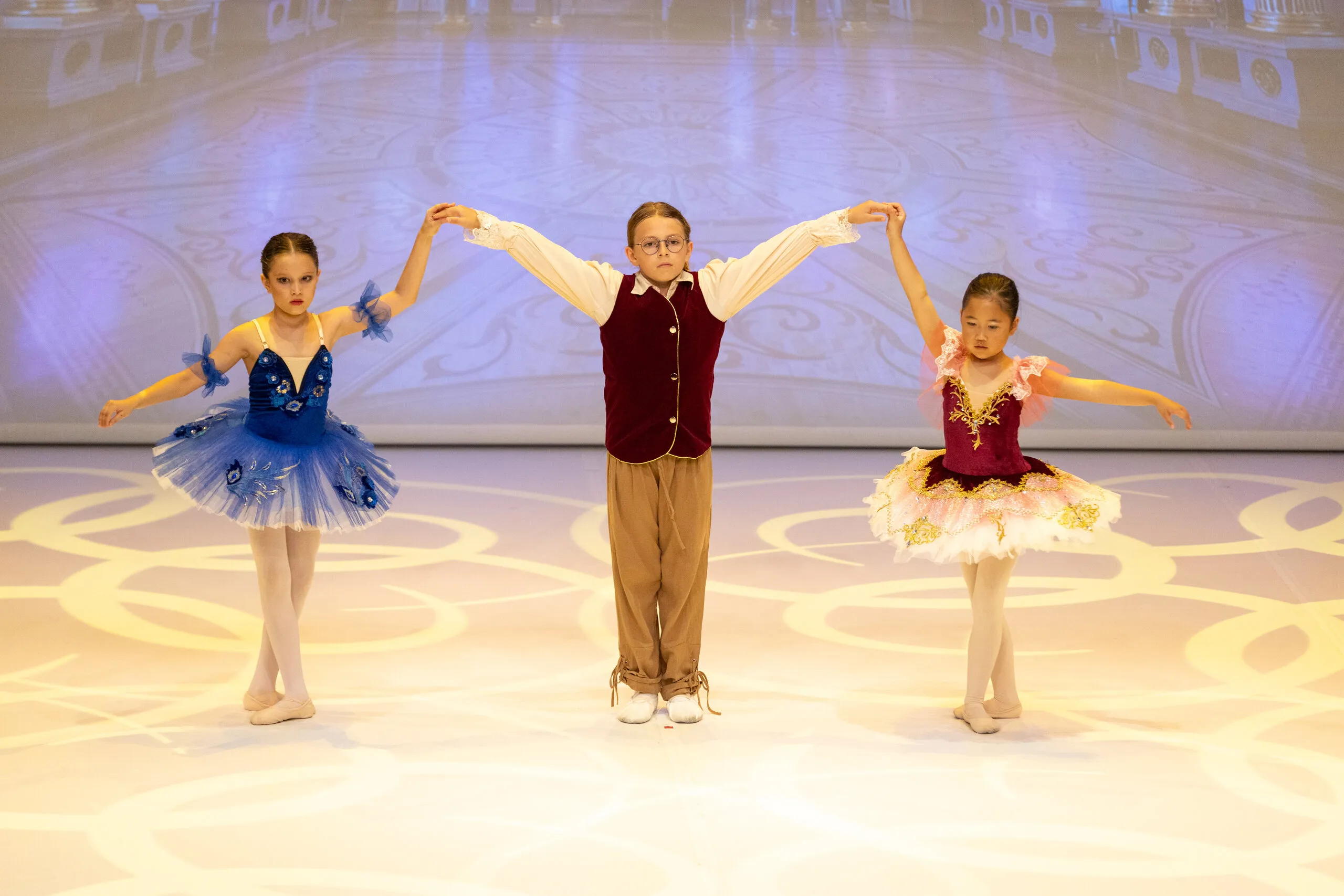 Three young students hand in hand, in blue and burgundy tutus.
