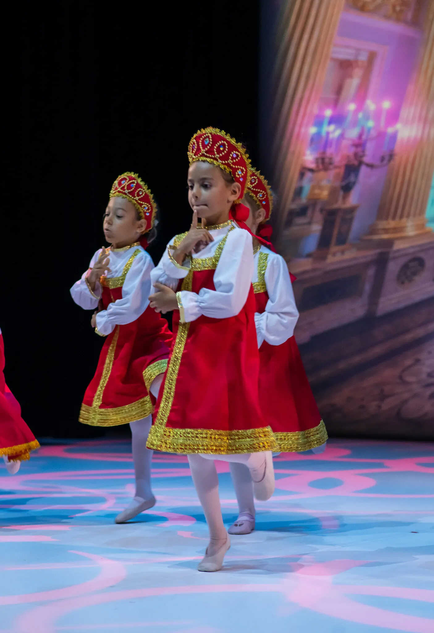 Two young students in red and gold costumes crossing the stage during the dress rehearsal.