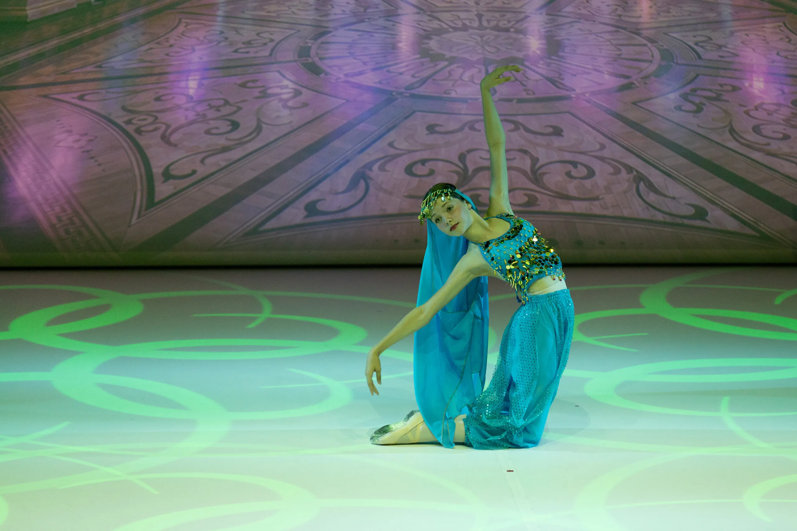 The Arabian dance, kneeling in the green light, one arm raised.