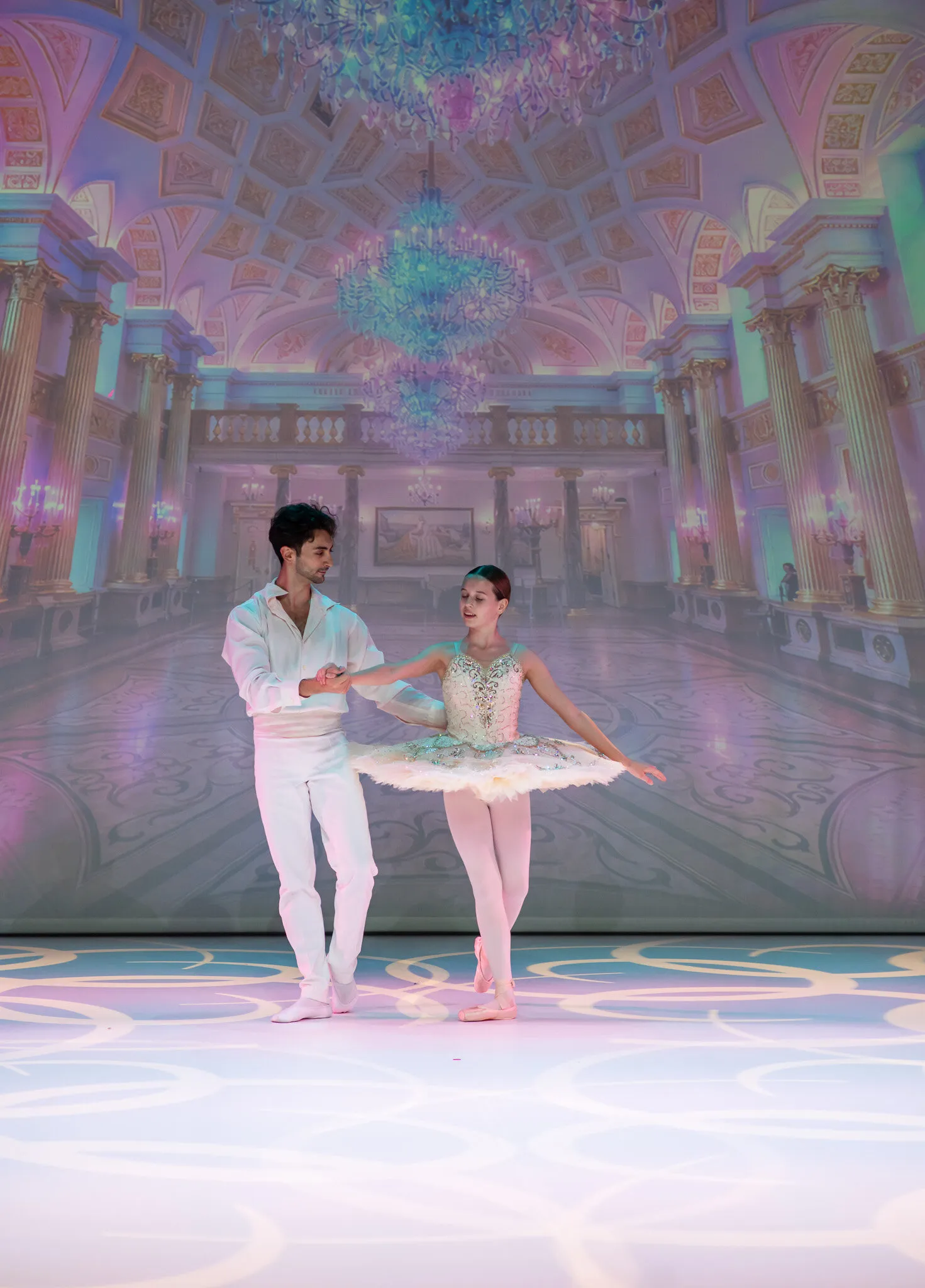 The young ballerina and her partner centre stage, the palace ballroom projected behind them.