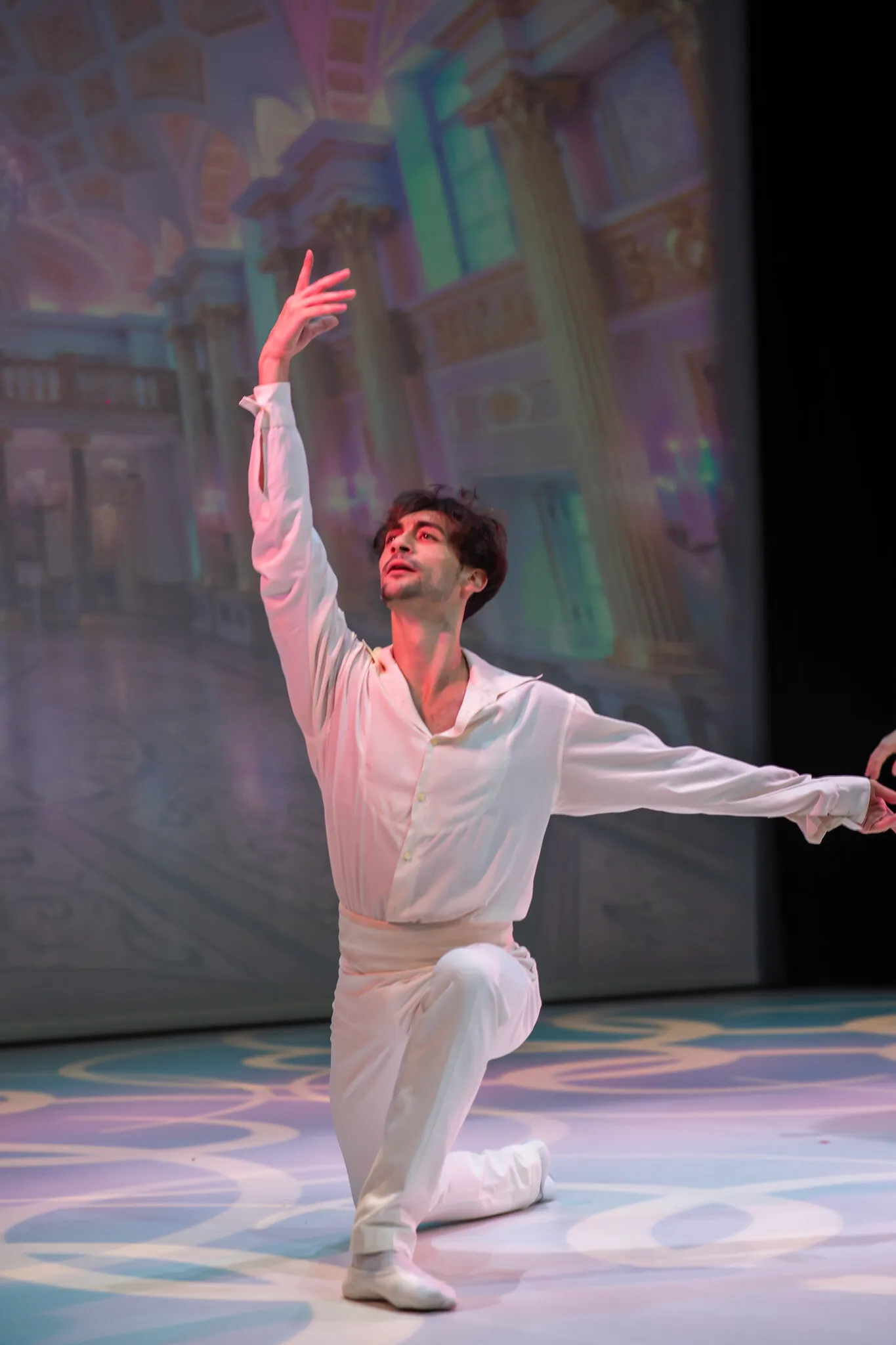 The dancer in white alone, one knee to the floor and one arm raised, before the palace set.