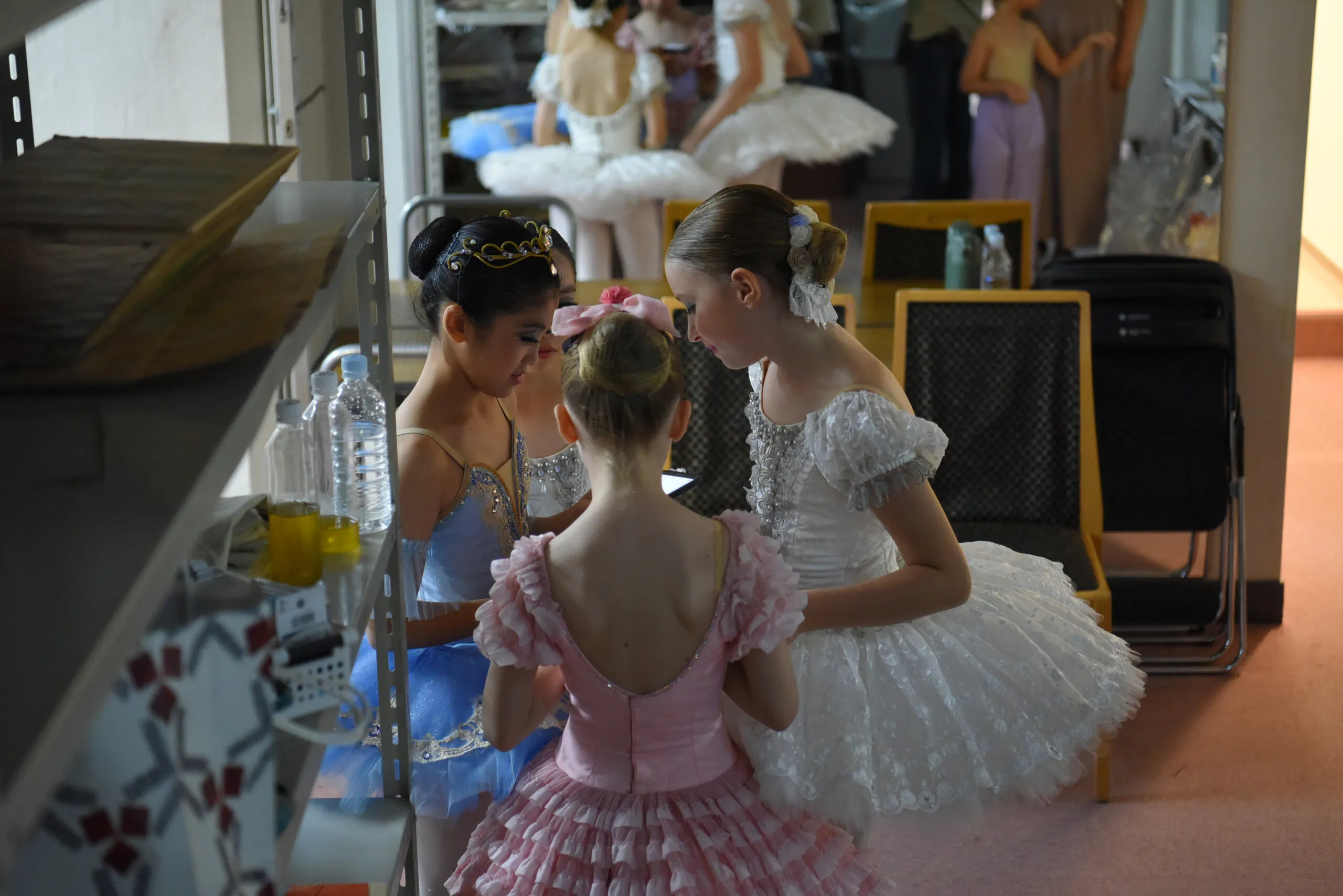 Quatre élèves en tutus, tête contre tête, dans les coulisses.