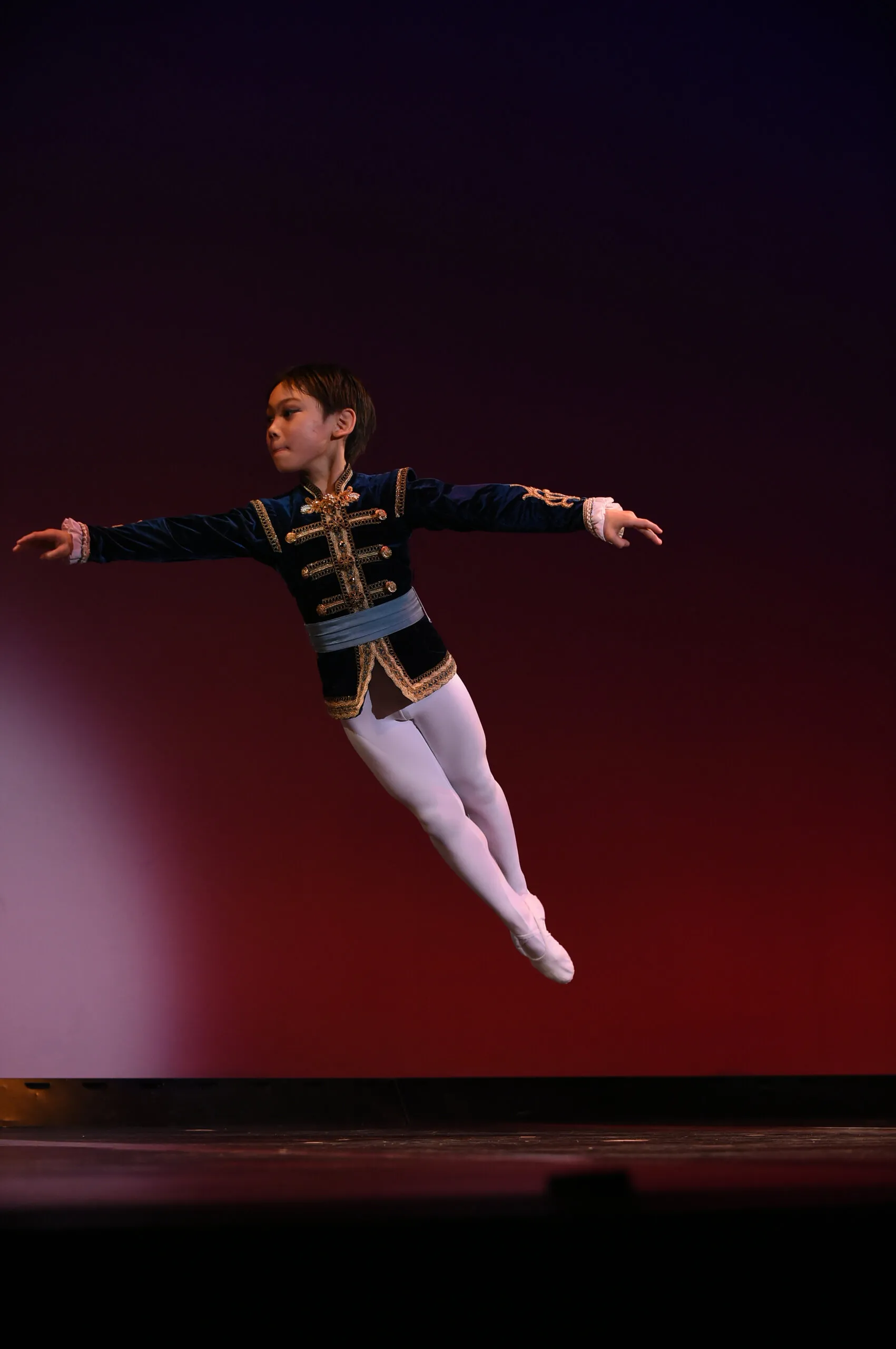 Un jeune danseur en plein saut, costume de velours bleu.