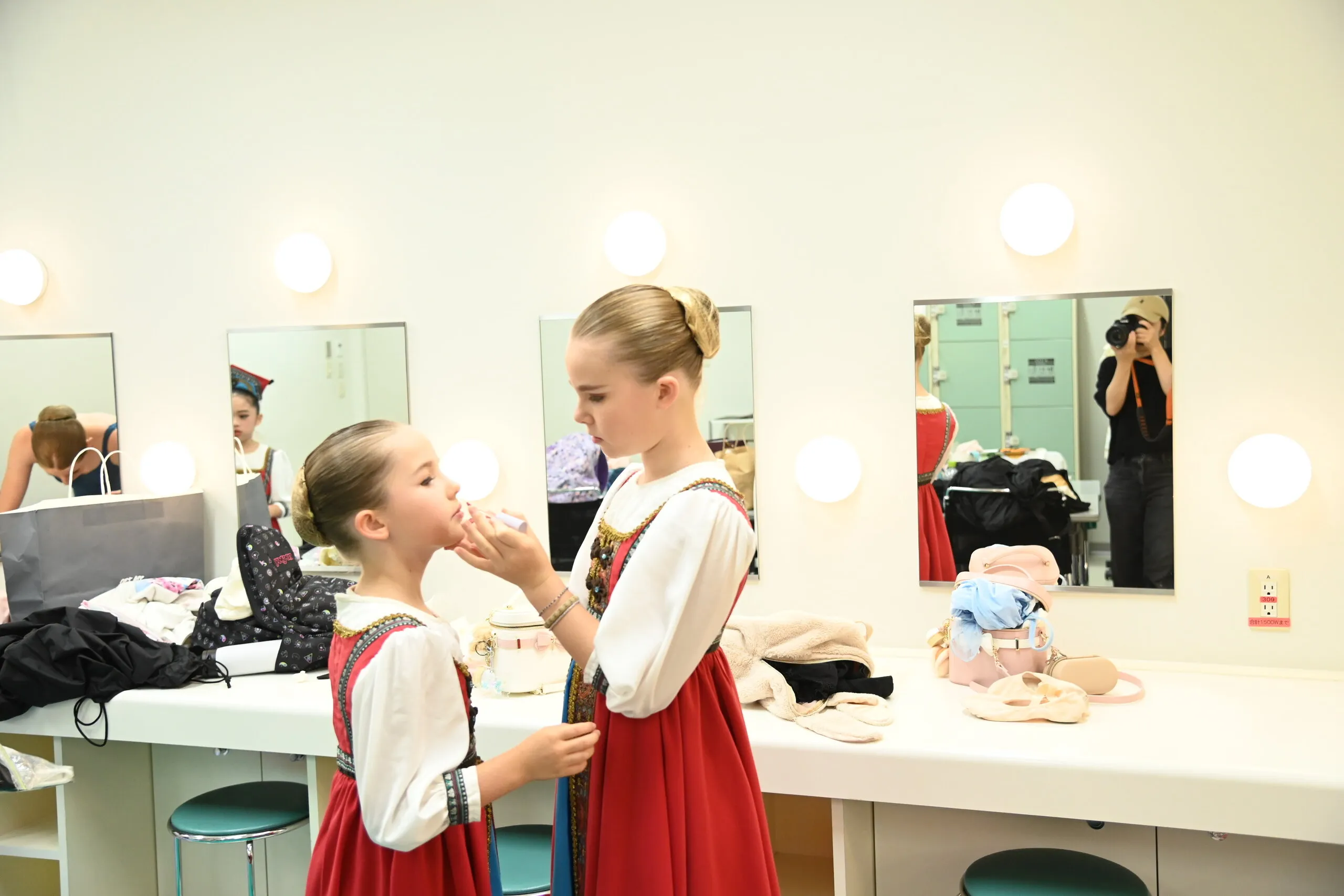 A view of the dressing room, an older student doing a younger one's make-up in front of the mirrors.