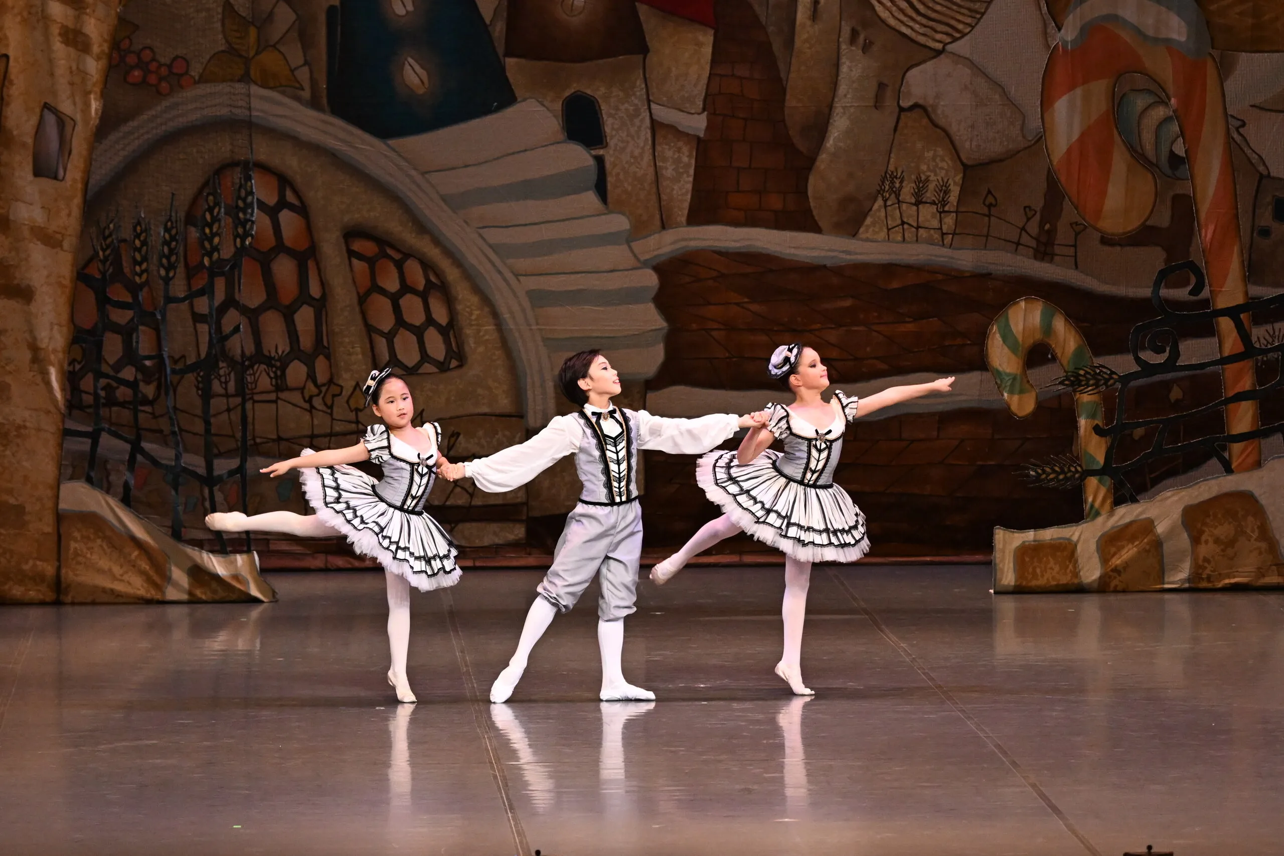 Trio d'élèves en costumes noir et blanc, arabesques main dans la main.