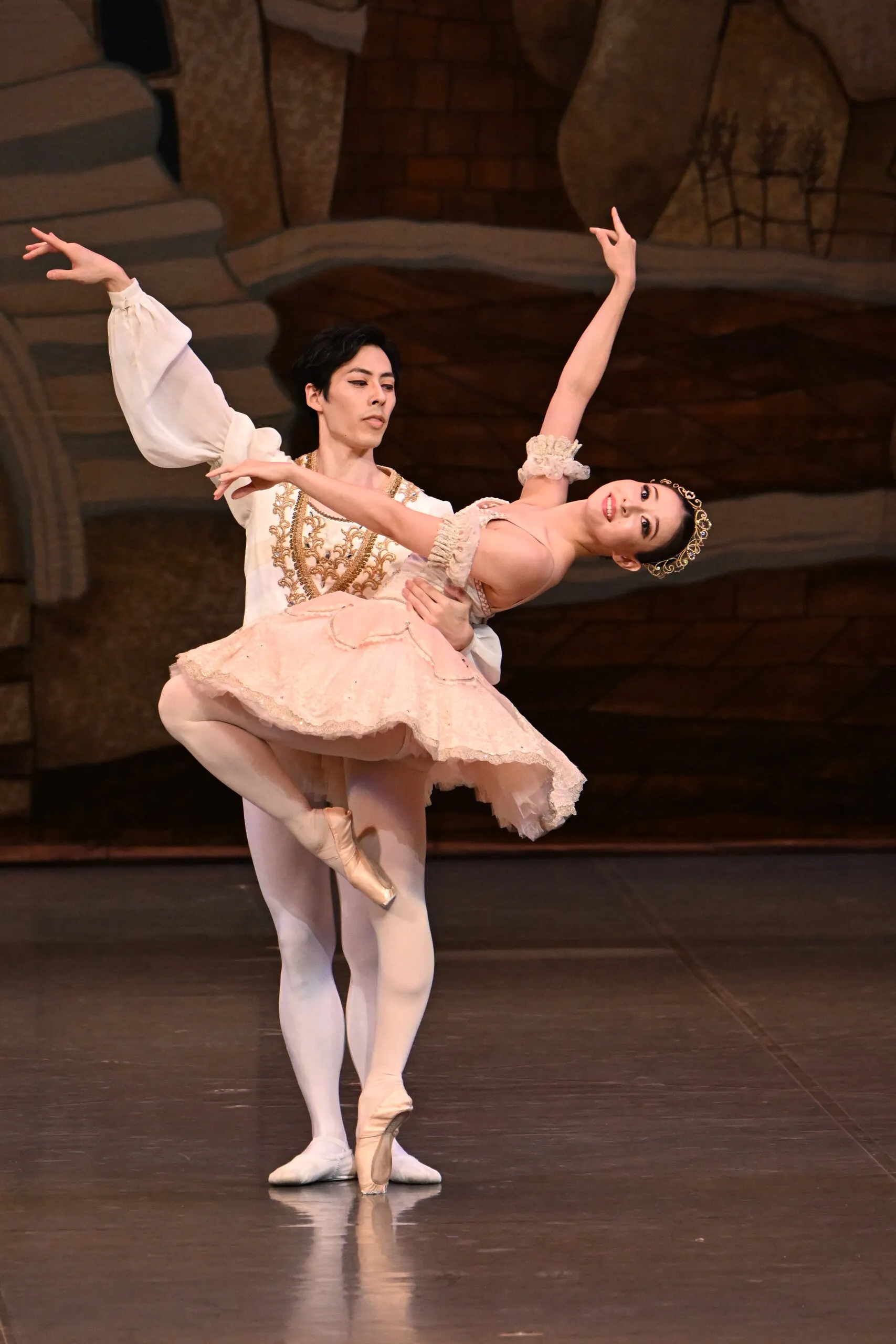 Pas de deux en tutu pêche, la danseuse en retiré soutenue par son partenaire.