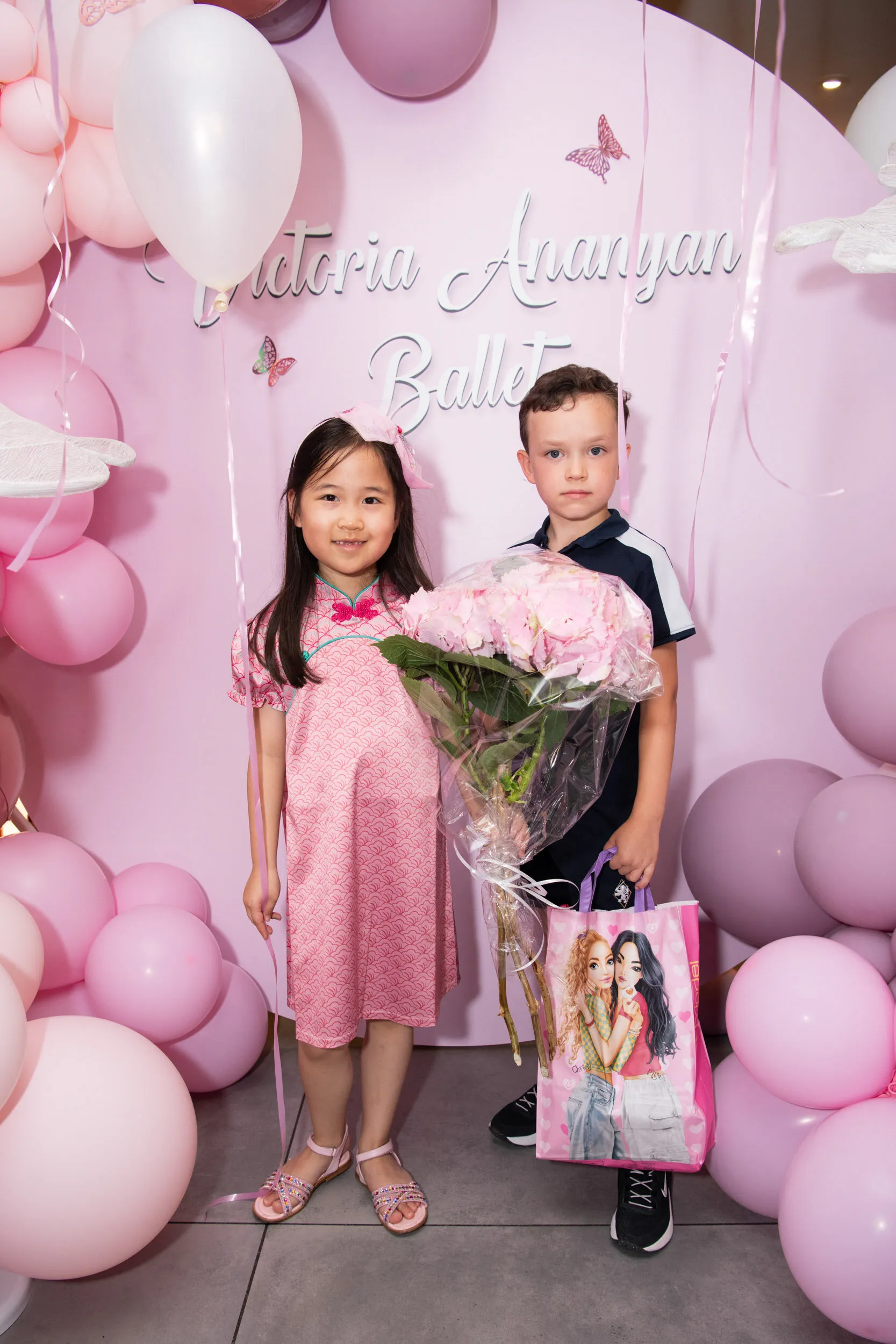 A student and a young guest with a bouquet of hydrangeas in front of the party backdrop.