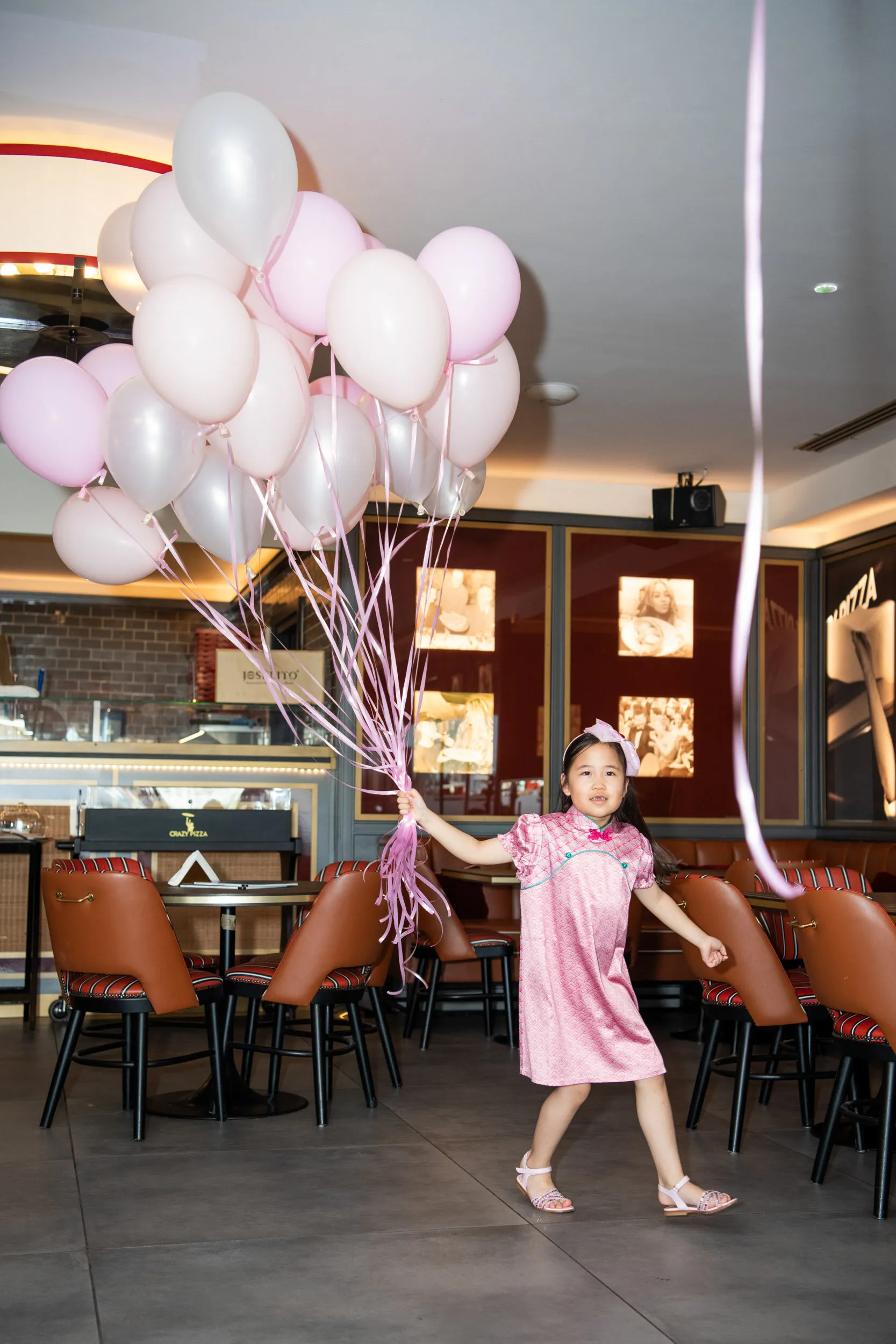 A child crosses the room with a large bunch of pink balloons.