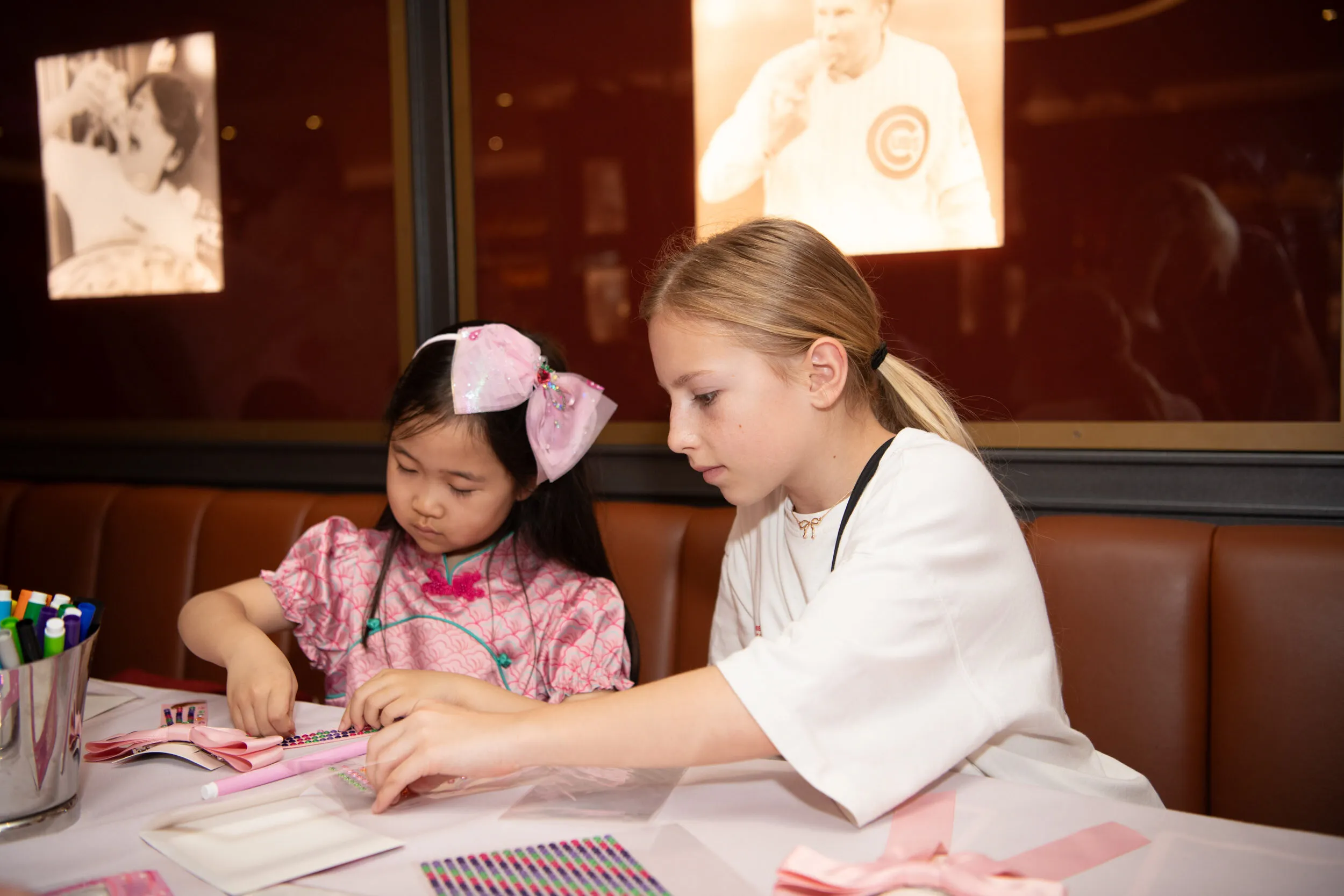 Two children put together ribbons and sticker gems at the workshop table.