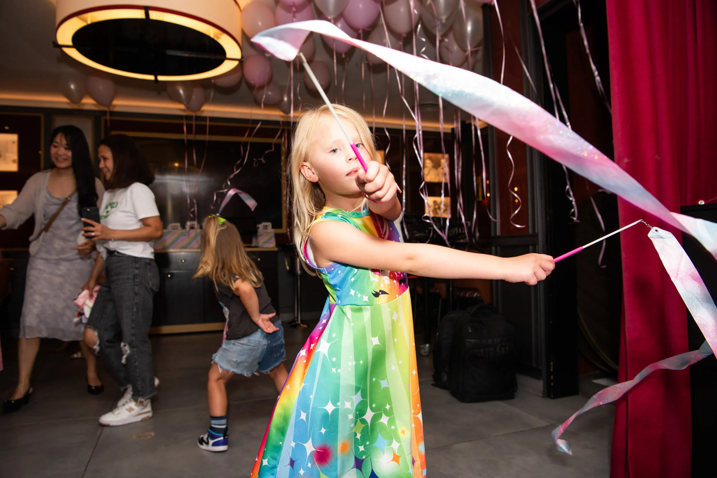 A child swirls two long ribbons in the balloon filled room.