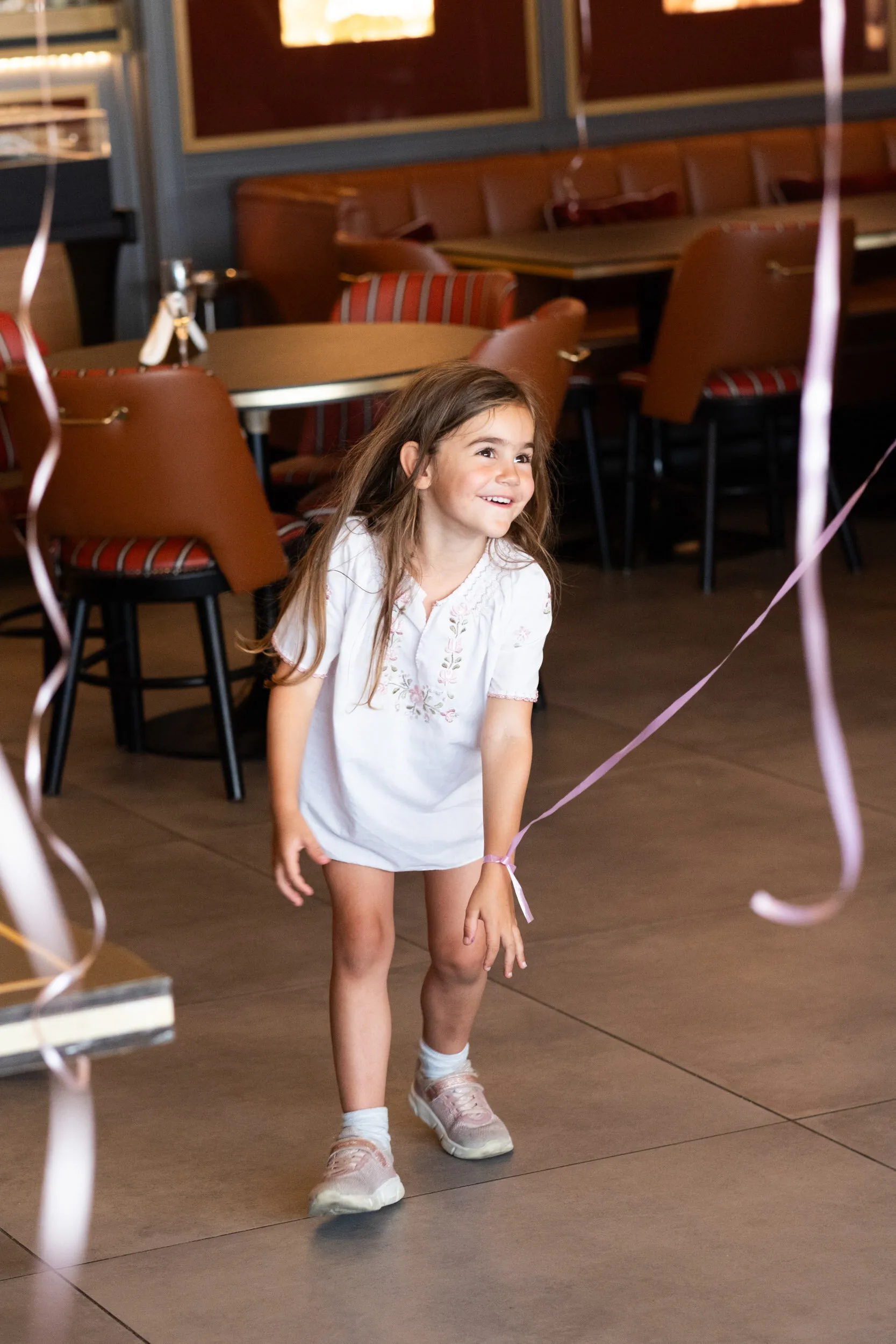 A child laughs while dancing, a balloon ribbon tied to her wrist.