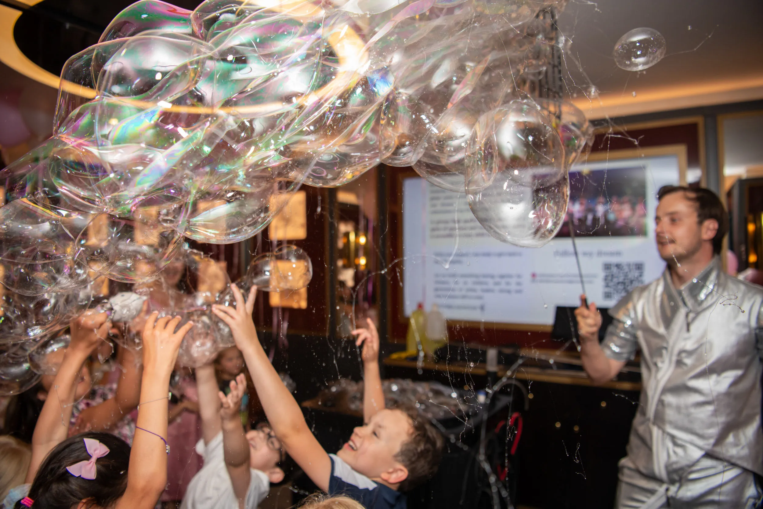 Children's hands reaching up into a cascade of iridescent bubbles.