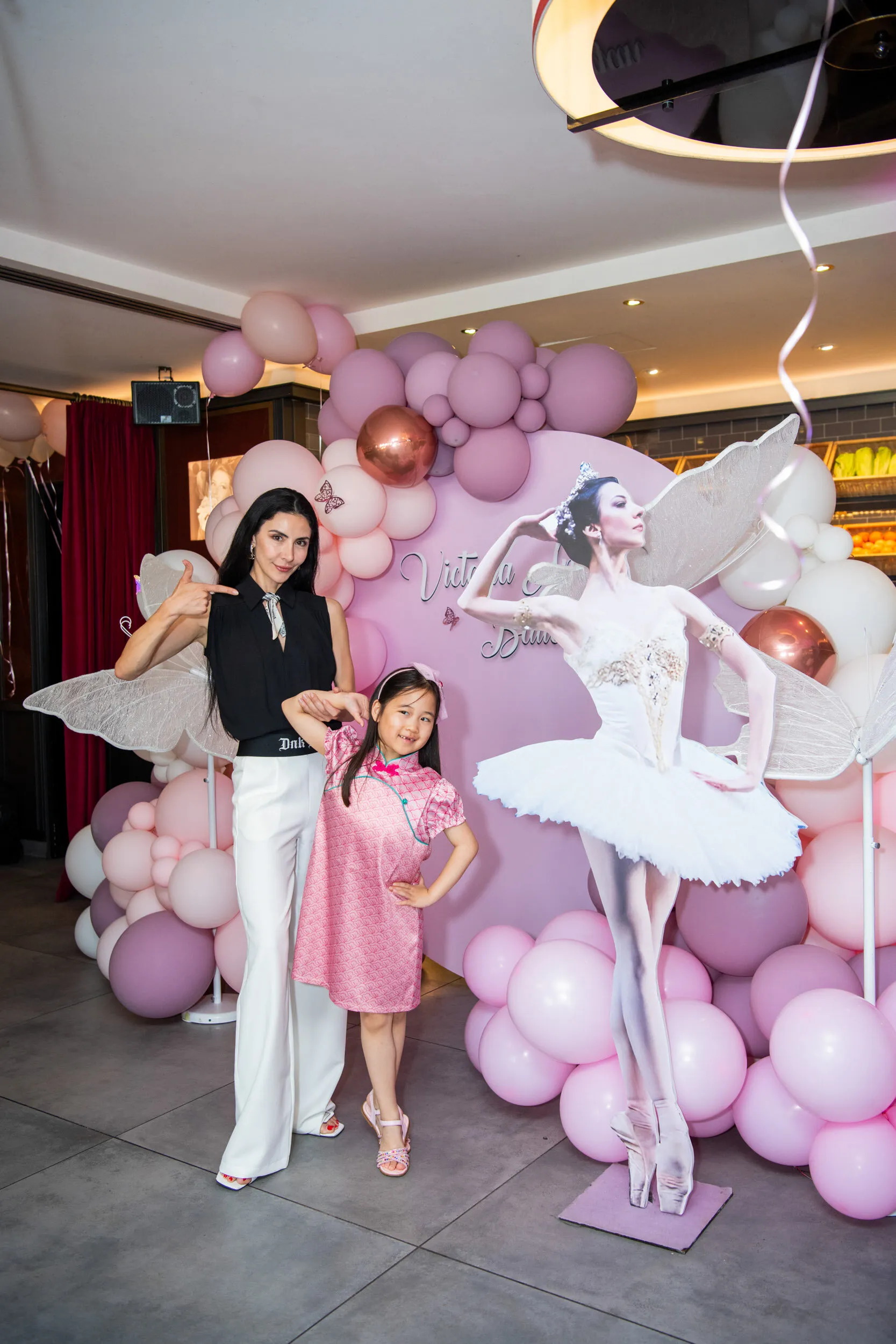 The founder and a young student beside the ballerina figure, under the pink balloons.