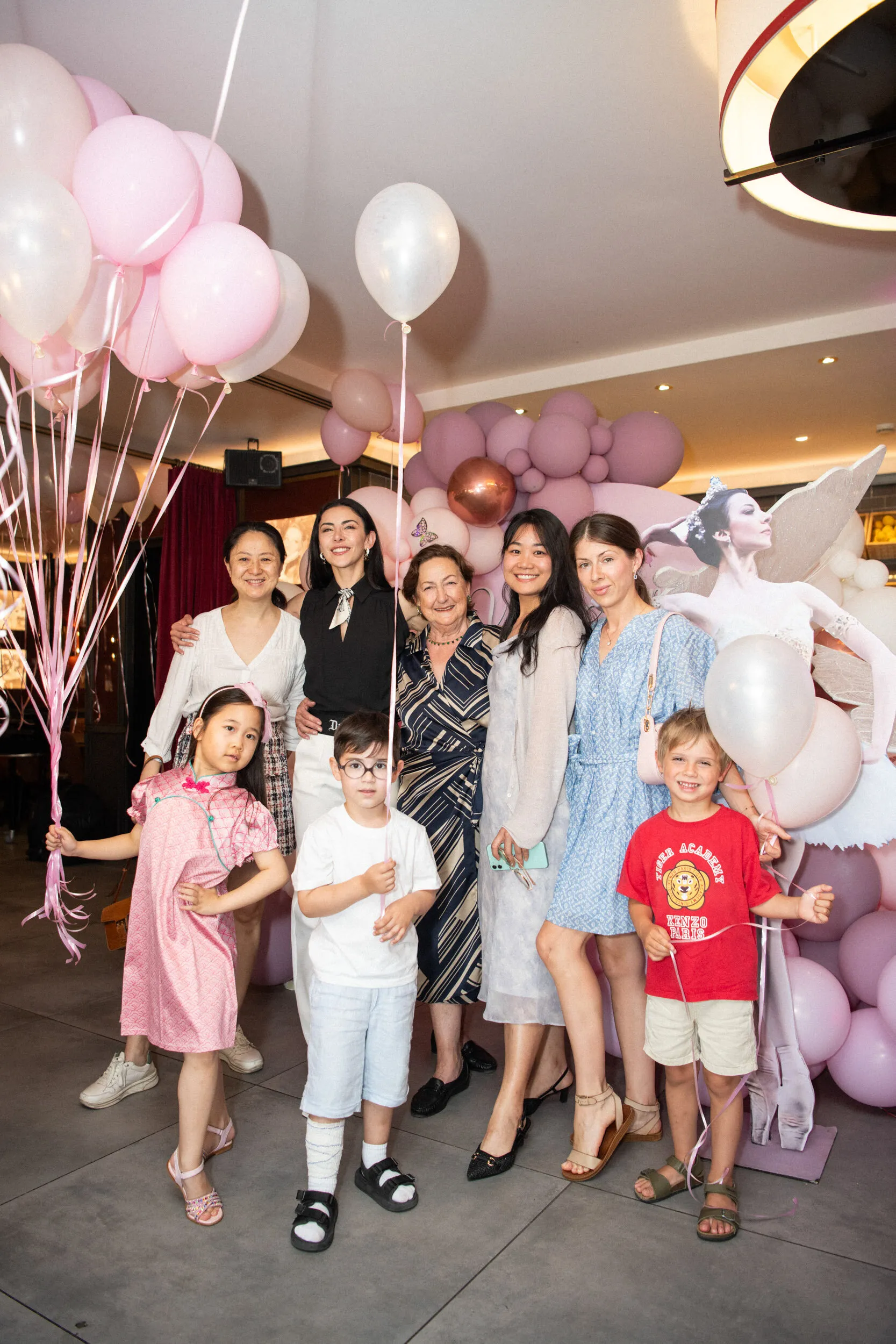 The founder and guests pose with three children under the cluster of pink balloons.