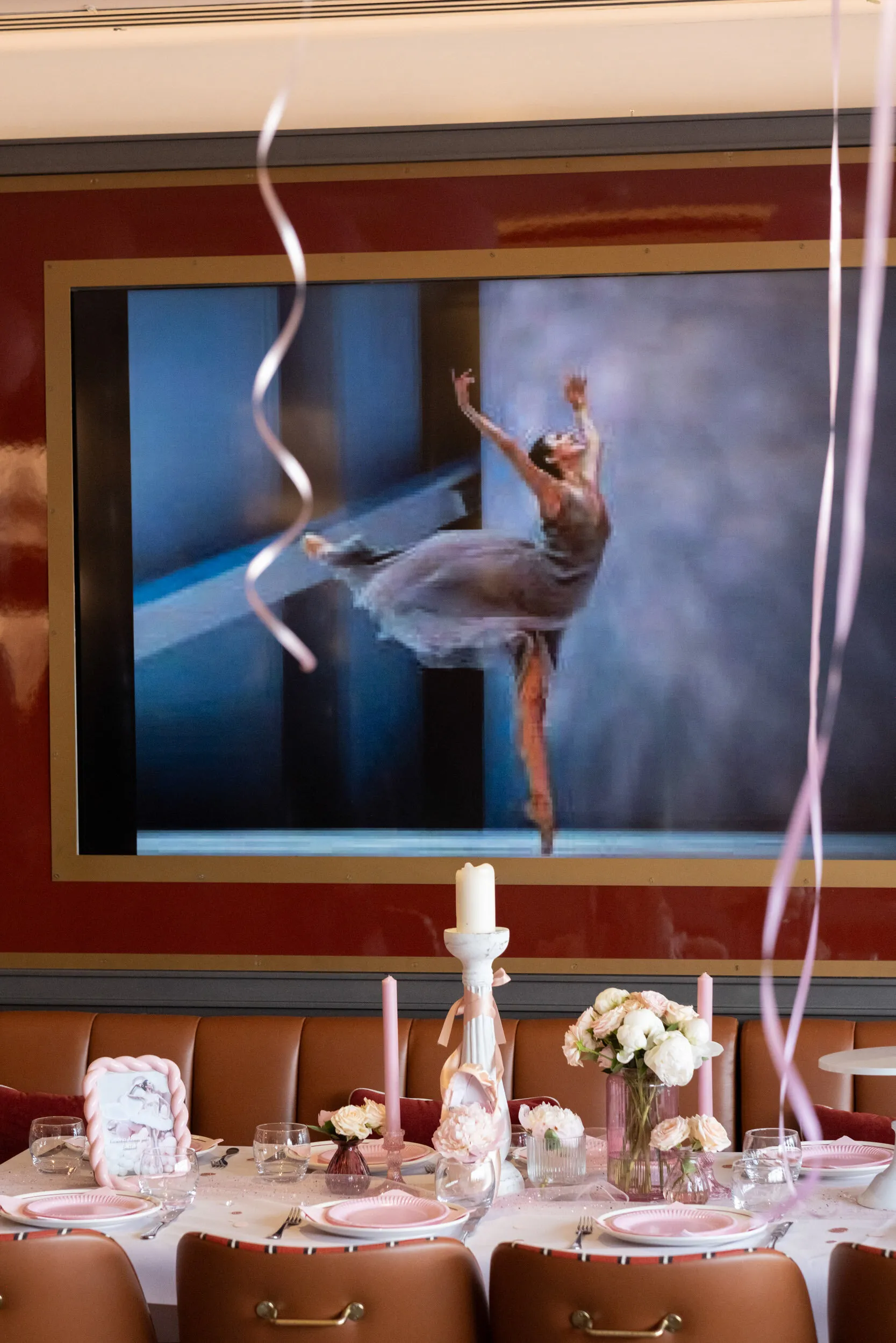A ballerina on the screen above the table laid for the party, with candles and white flowers.