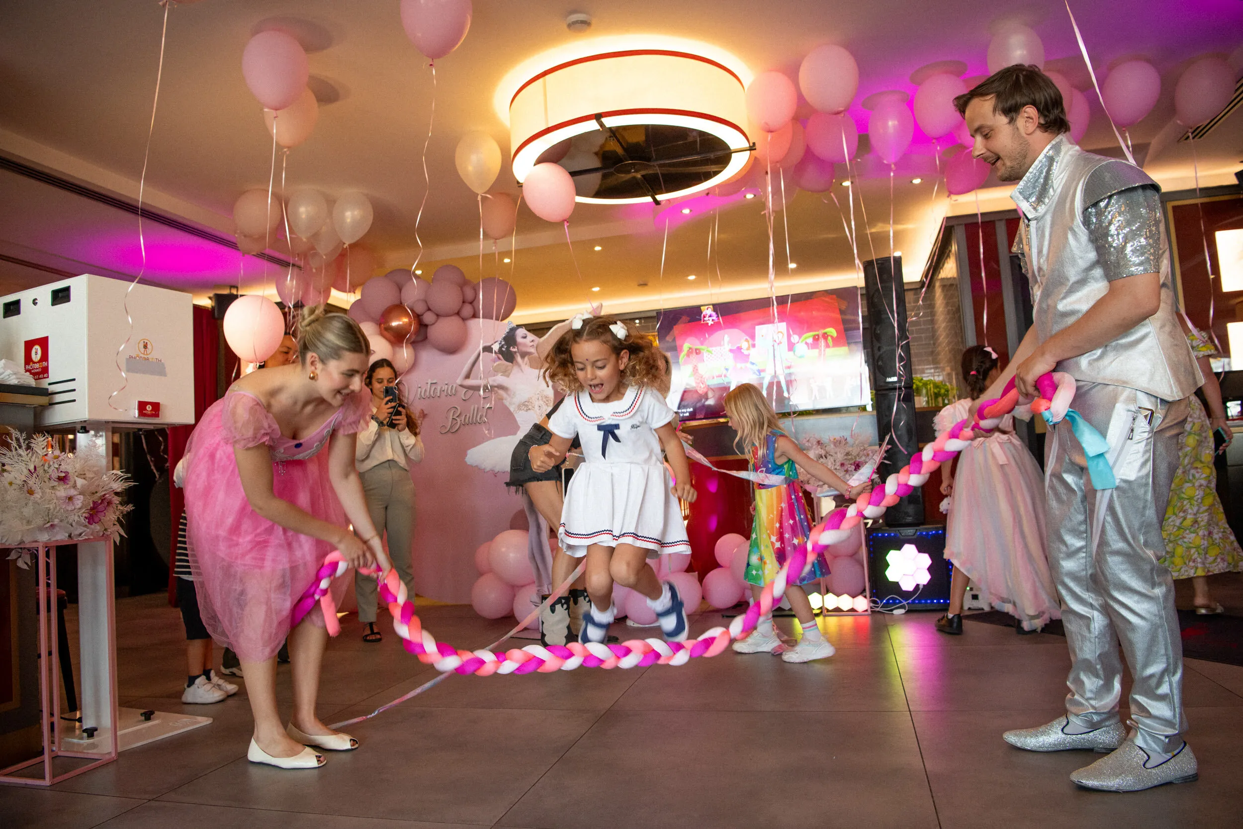Two performers hold the long braided rope while a child leaps over it.