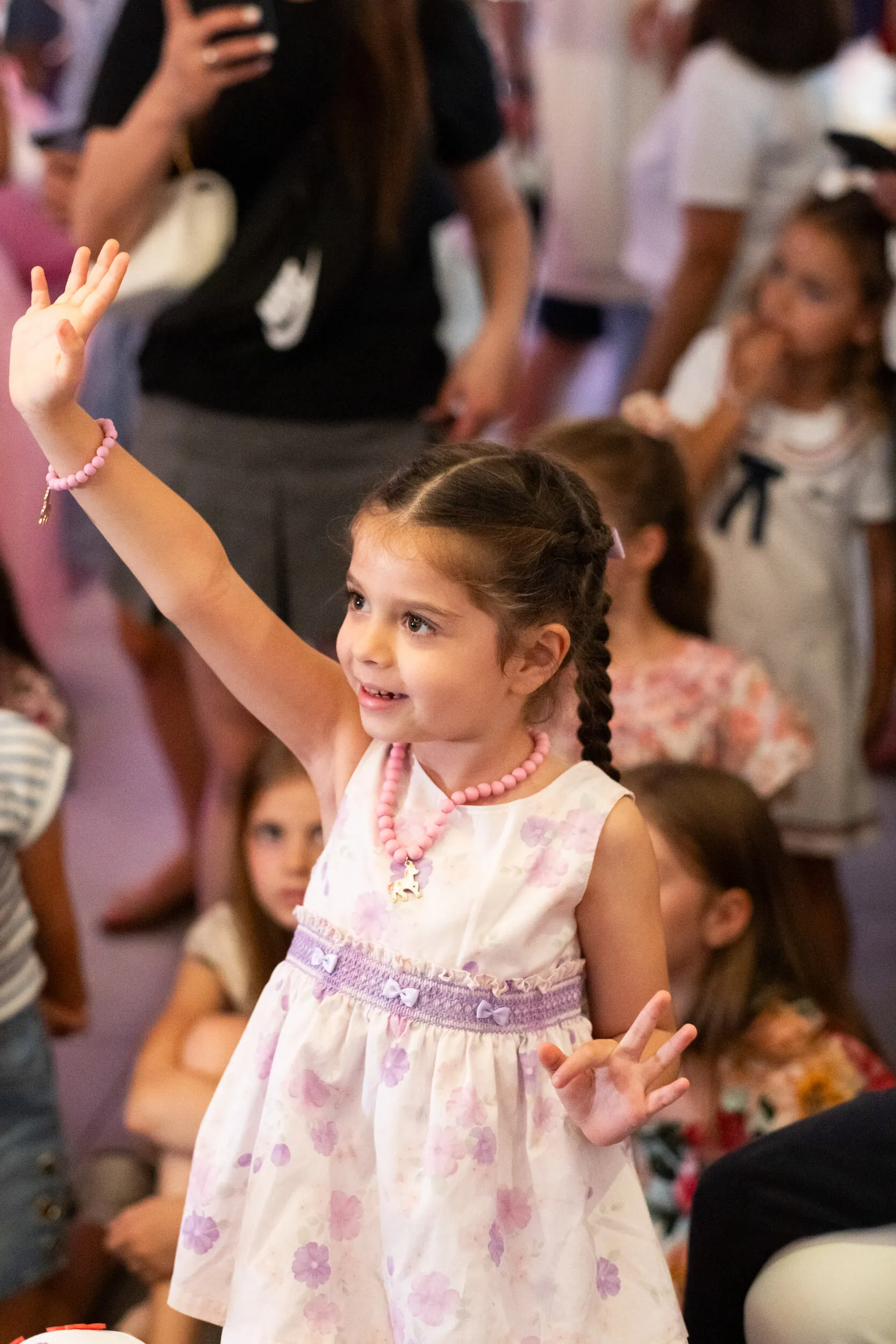 A child in the audience raises her hand, smiling.