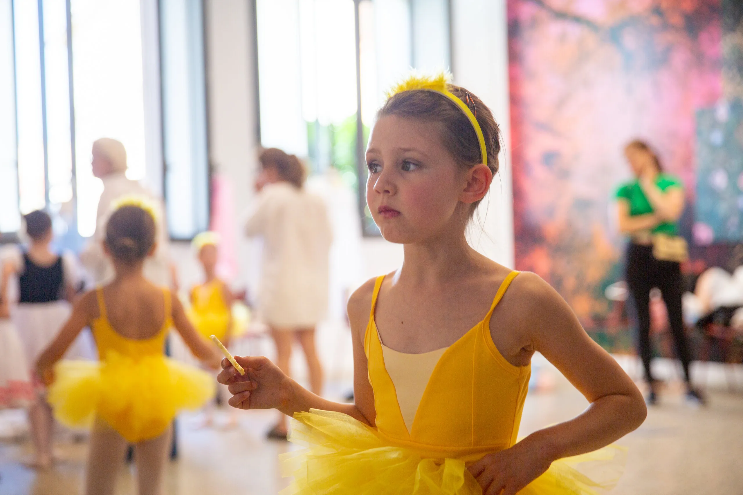 Une élève en tutu jaune, main sur la hanche, dans le hall avant son passage.