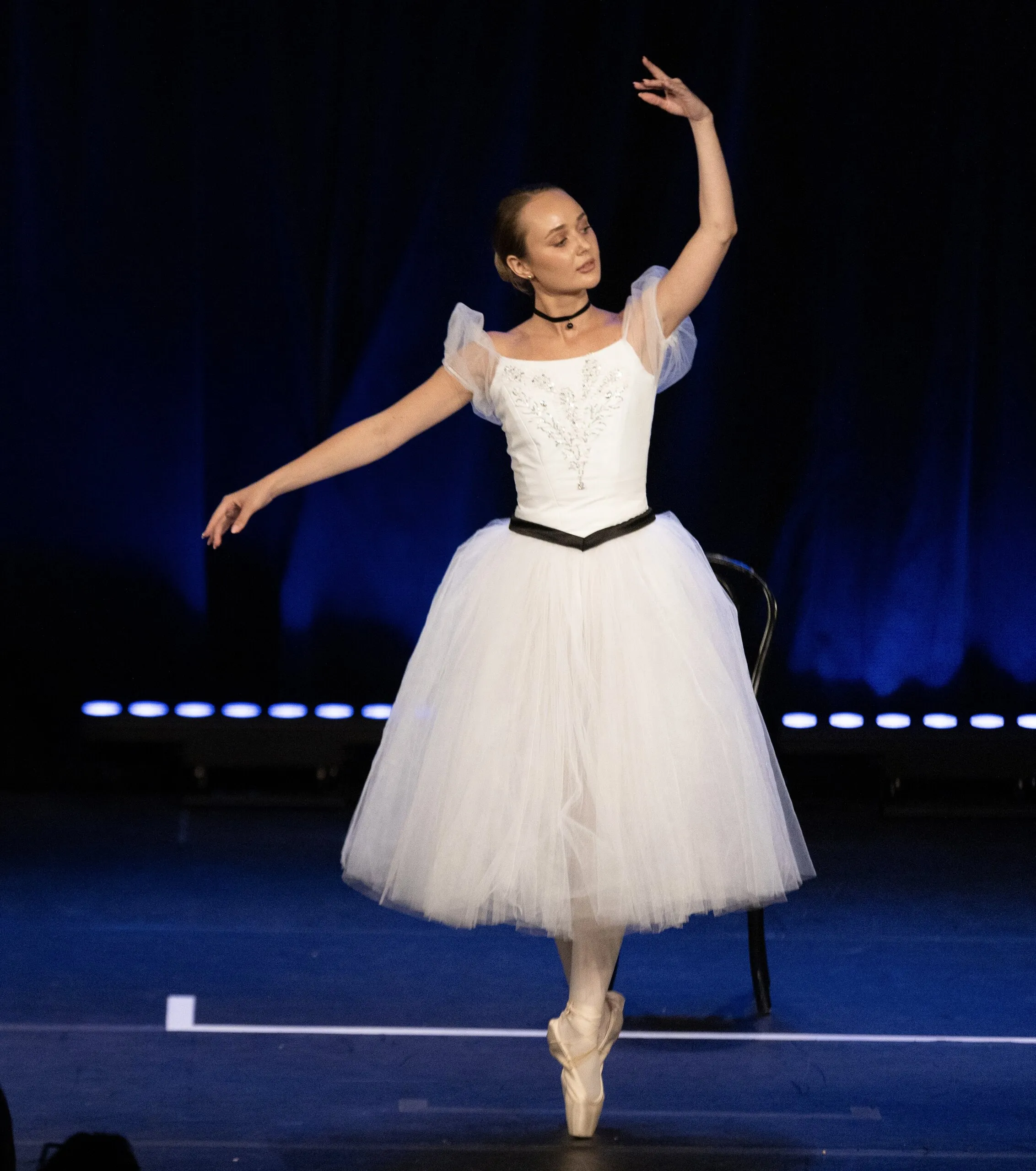 Une soliste en long tutu blanc, sur pointes, sur le plateau bleu.