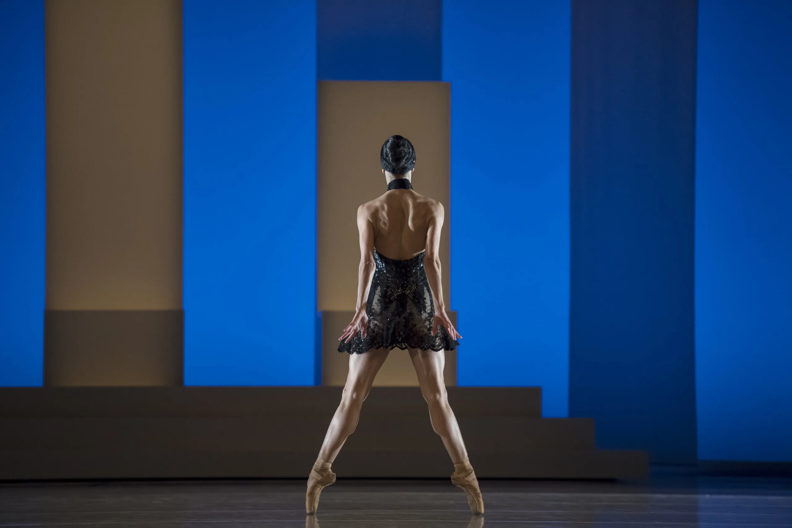 Une danseuse de dos sur pointes, entre les colonnes bleues du décor, sur la scène des Ballets de Monte-Carlo.