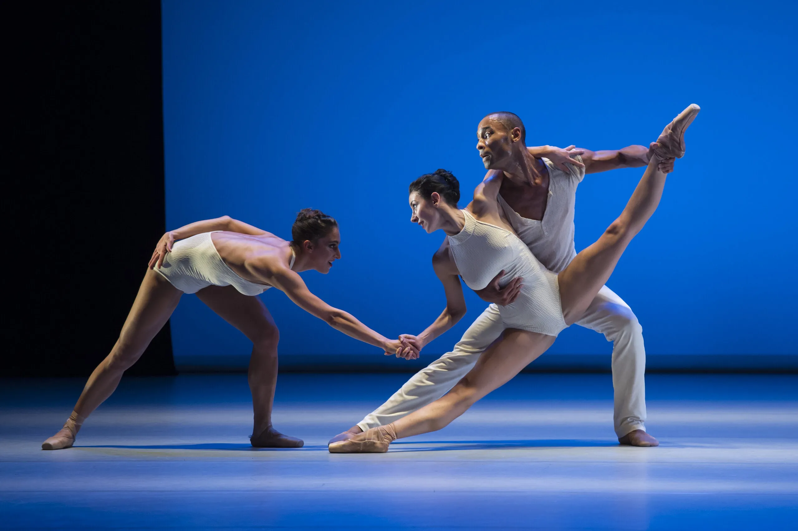 Victoria en équilibre soutenue par un danseur, la main tendue vers une danseuse penchée, sur une scène bleue.