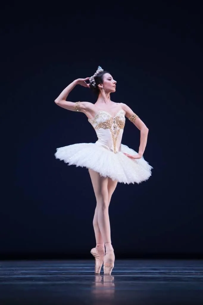 Victoria en tutu blanc et diadème, sur pointes, devant un fond bleu nuit.