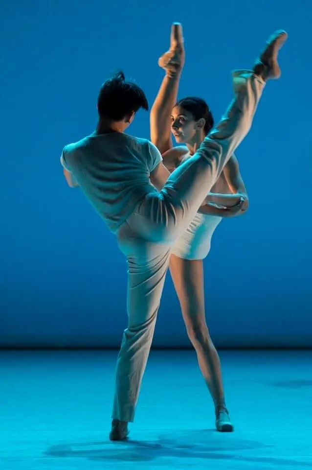 Victoria et son partenaire en costumes turquoise, la jambe haute, sur une scène bleue.
