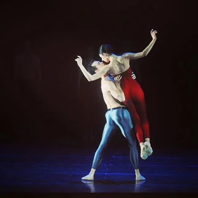 Pas de deux contemporain, Victoria dans les bras de son partenaire, sur une scène sombre.