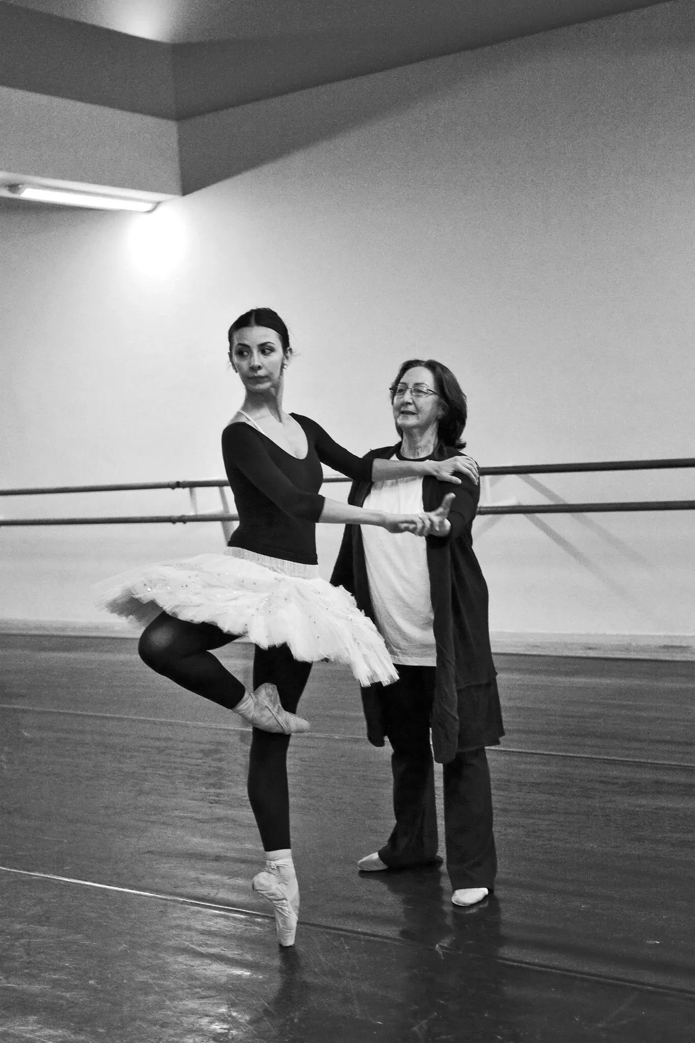 Victoria en tutu blanc à la barre, la main tenue par une professeure, en studio.