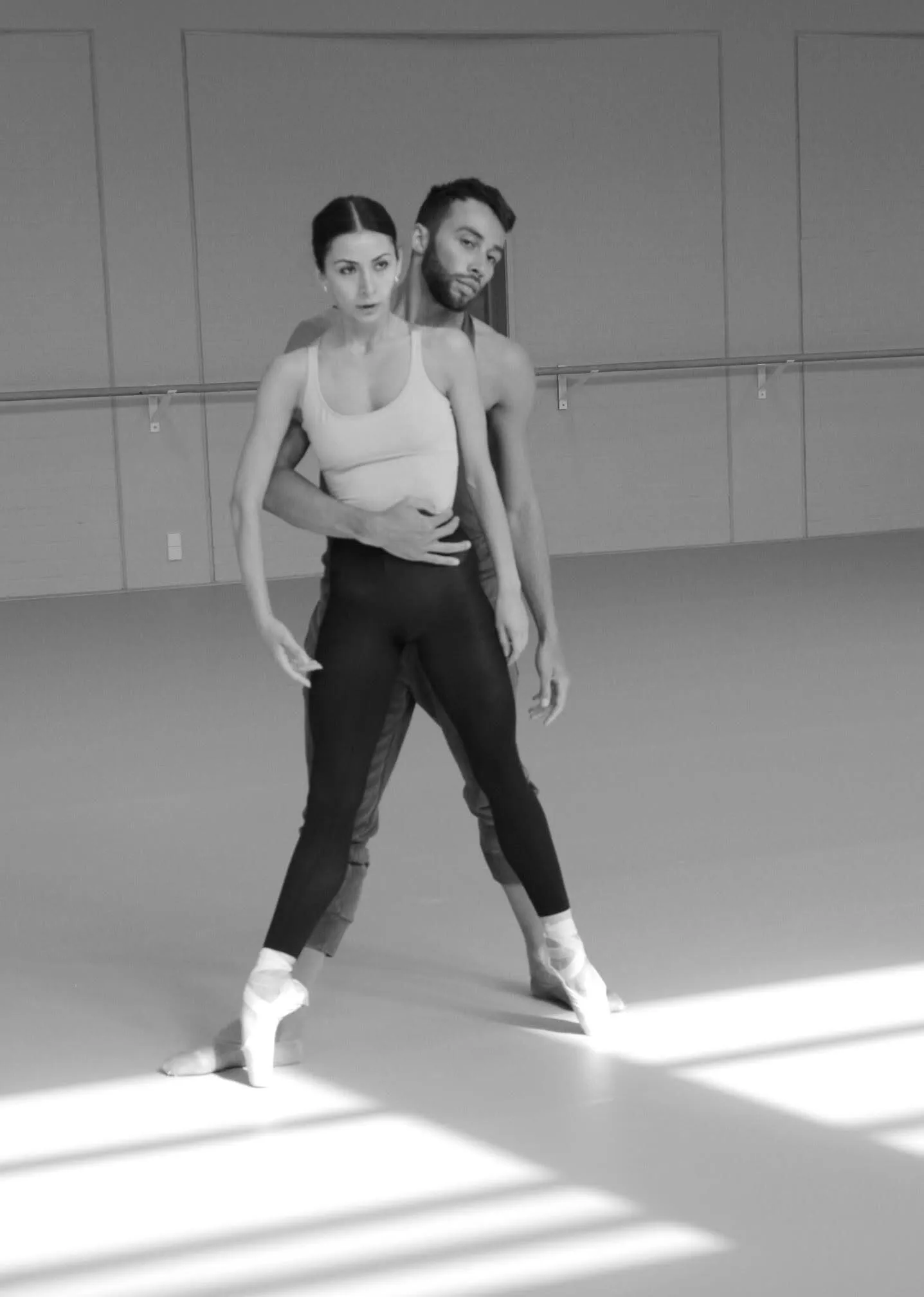 Répétition d'un pas de deux dans un studio traversé de soleil, en noir et blanc.
