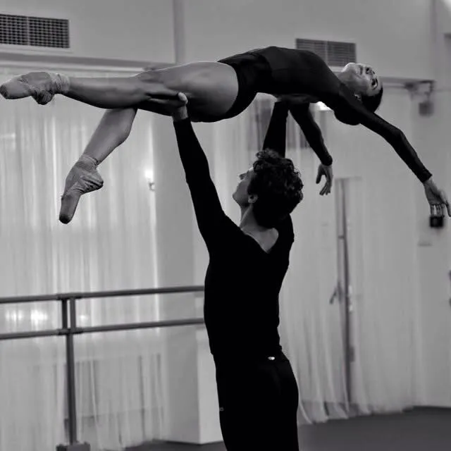 Une danseuse portée à l'horizontale au-dessus des épaules de son partenaire, en studio.